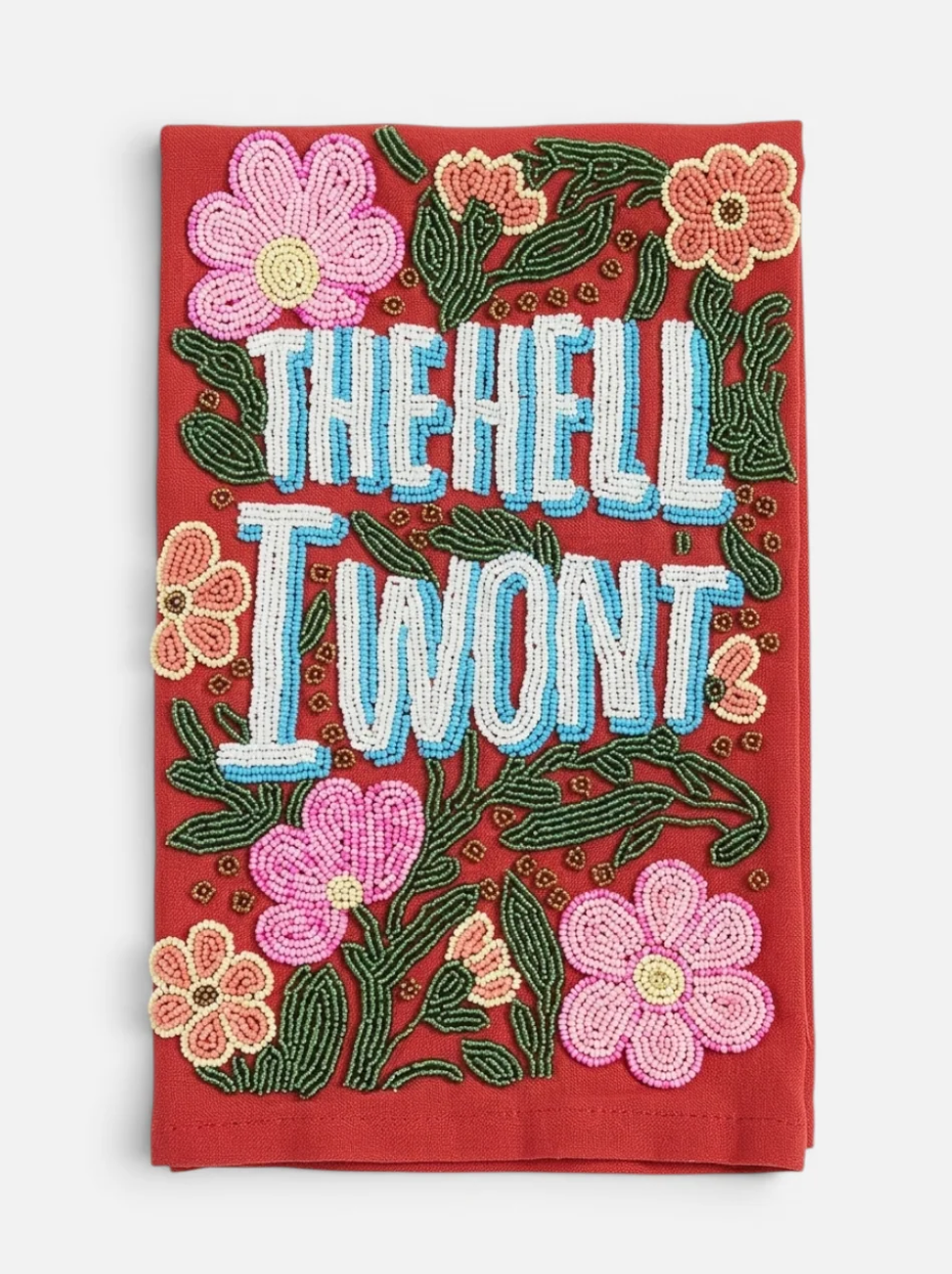 A red fabric tea towel featuring the phrase 'THE HELL I WONT' in large white letters with light blue outlines, surrounded by pink and peach flowers and green leaves.